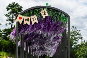 Black garden arch adorned with purple lavender flowers and Korean text bunting flags against a cloudy sky.