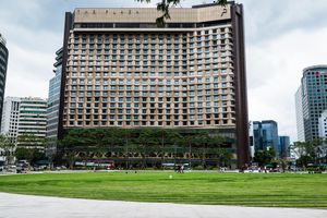 Large modern hotel building with grid-like facade overlooking a lush green park in an urban city setting.