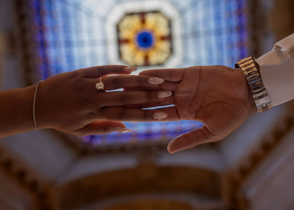 Two hands touching gently in a church with colorful stained glass windows in the background.