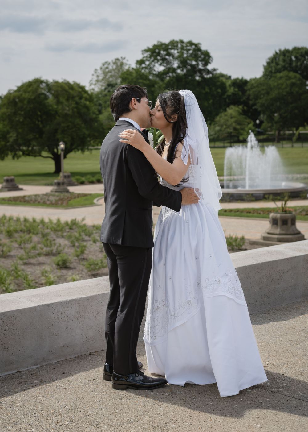 Bride and groom sharing a kiss in front of a garden fountain on their wedding day.