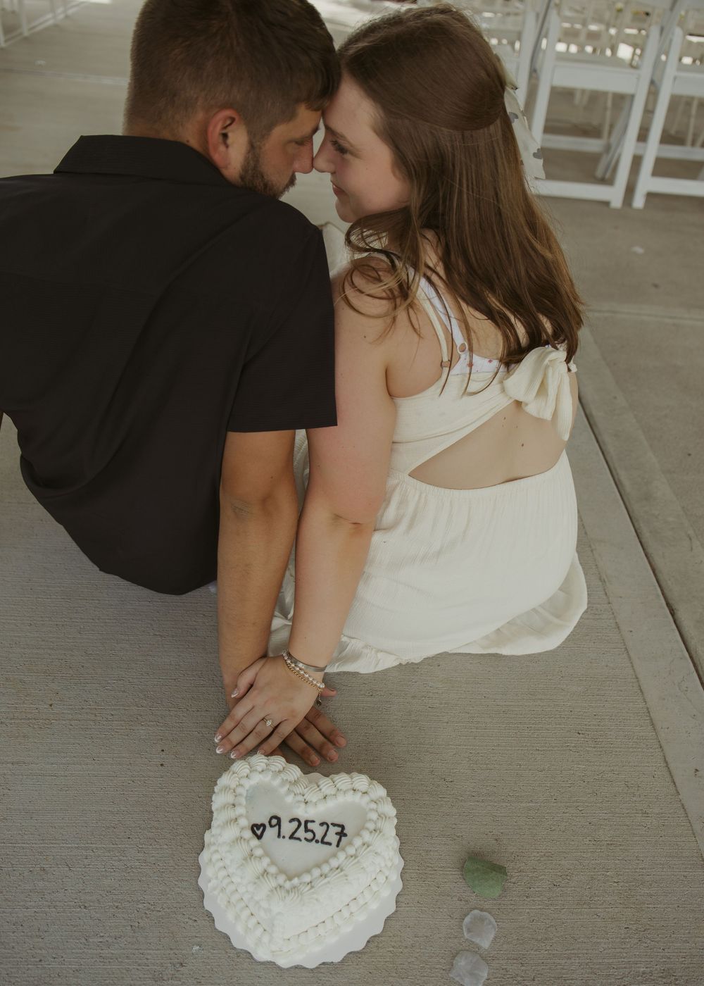 Couple sitting together touching foreheads over a heart-shaped engagement cake with date 9.25.27.