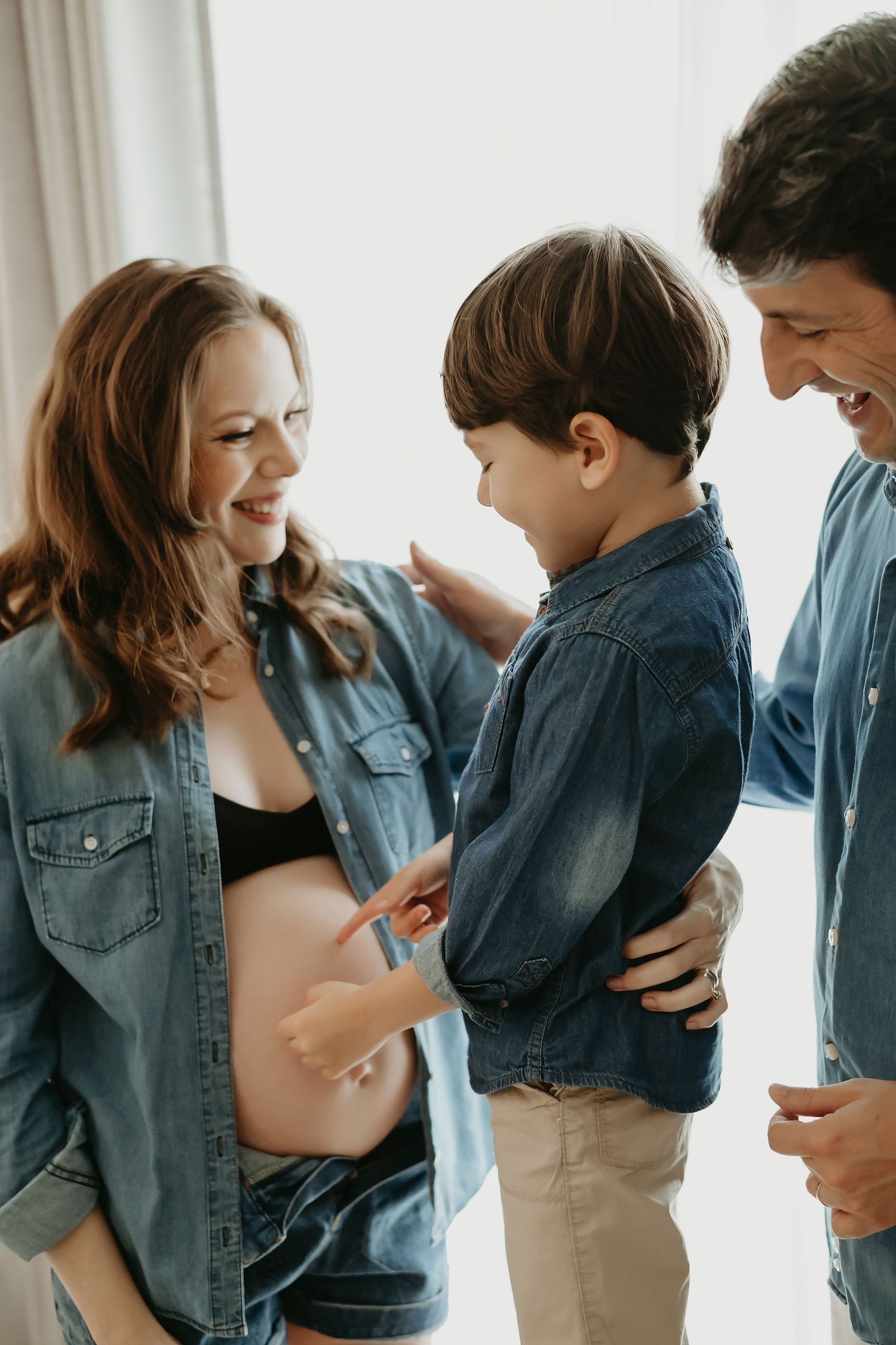 Pregnant woman with family, son touching baby bump, maternity photo session with parents in denim shirts.