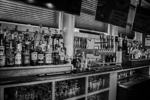Black and white bar interior with shelves of liquor bottles, beer taps, and glassware in a classic pub setting.