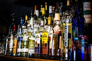 Colorful assortment of liquor bottles on a bar shelf, including gin, tequila, and whiskey, illuminated by ambient lighting.
