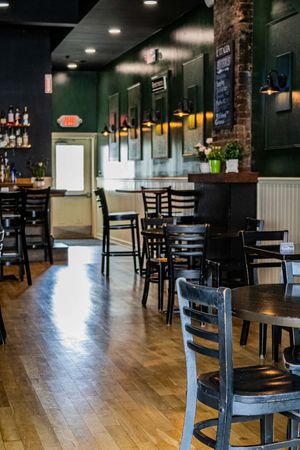 Cozy restaurant interior with dark wood chairs, hardwood floors, green walls, exposed brick, and a bar area with bottles.