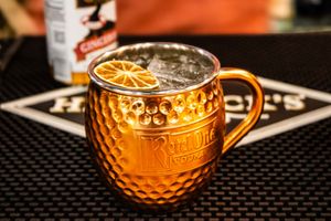Copper Moscow Mule mug with ice and orange slice garnish on a branded bar mat.
