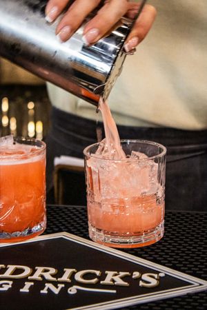 Bartender pouring a pink cocktail from a shaker into a rocks glass over ice at a Hendrick's Gin bar.