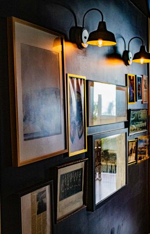 Dark gallery wall with framed artwork and vintage photos illuminated by industrial black sconce lights.