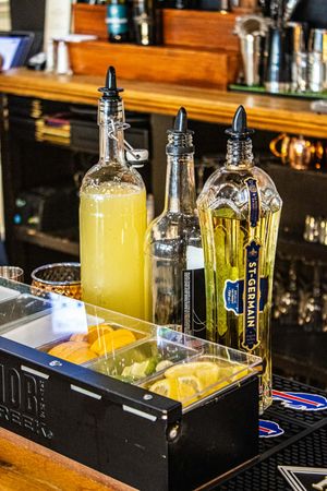Bar setup with St-Germain elderflower liqueur, fresh citrus garnishes, and cocktail bottles on a black tray.