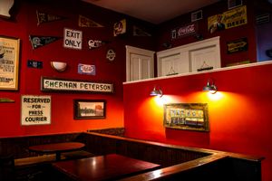 Vintage bar interior with red walls, retro signs, Sherman Peterson reserved sign, and Coca-Cola advertisements.