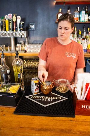 Bartender preparing cocktails at a Hendrick's Gin bar mat, with bottles and a copper mug on the counter.