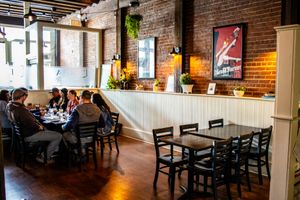Cozy brick-walled restaurant dining room with dark wood chairs, tables, and warm lighting, guests enjoying a meal together.