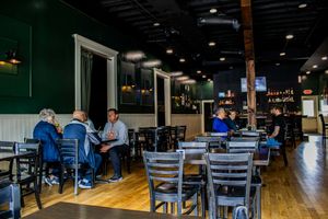 Casual restaurant interior with dark green walls, wood floors, and patrons dining under recessed lighting.