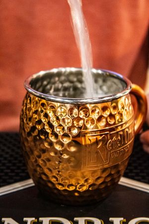 Liquid pouring into a hammered copper Moscow Mule mug with Ketel One Vodka branding on a dark surface.