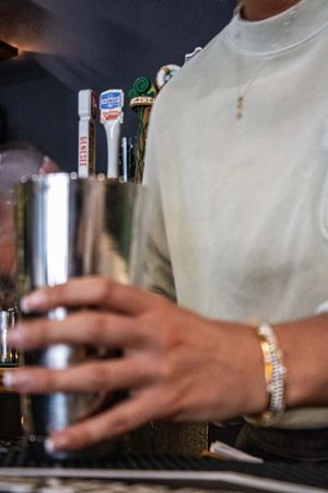 Bartender in white turtleneck holding a cocktail shaker near Guinness beer taps at a bar.