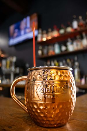 Ketel One vodka Moscow Mule cocktail in a copper mug with a straw, served at a bar.