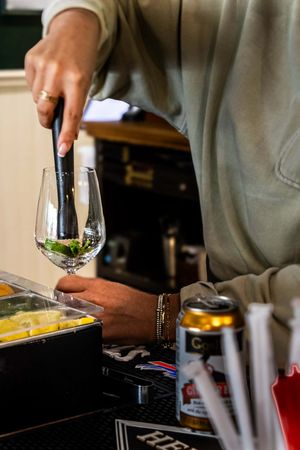 Bartender placing fresh mint into a wine glass while preparing a cocktail at a bar with beer cans nearby.