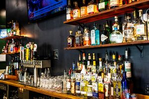 Well-stocked bar shelves lined with colorful liquor bottles and shot glasses, with beer taps visible at a wooden bar counter.