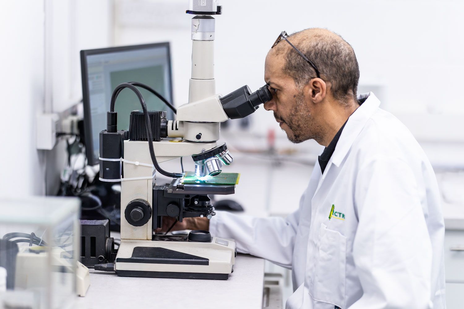 Scientist in white lab coat examining samples through a microscope in a modern laboratory setting.
