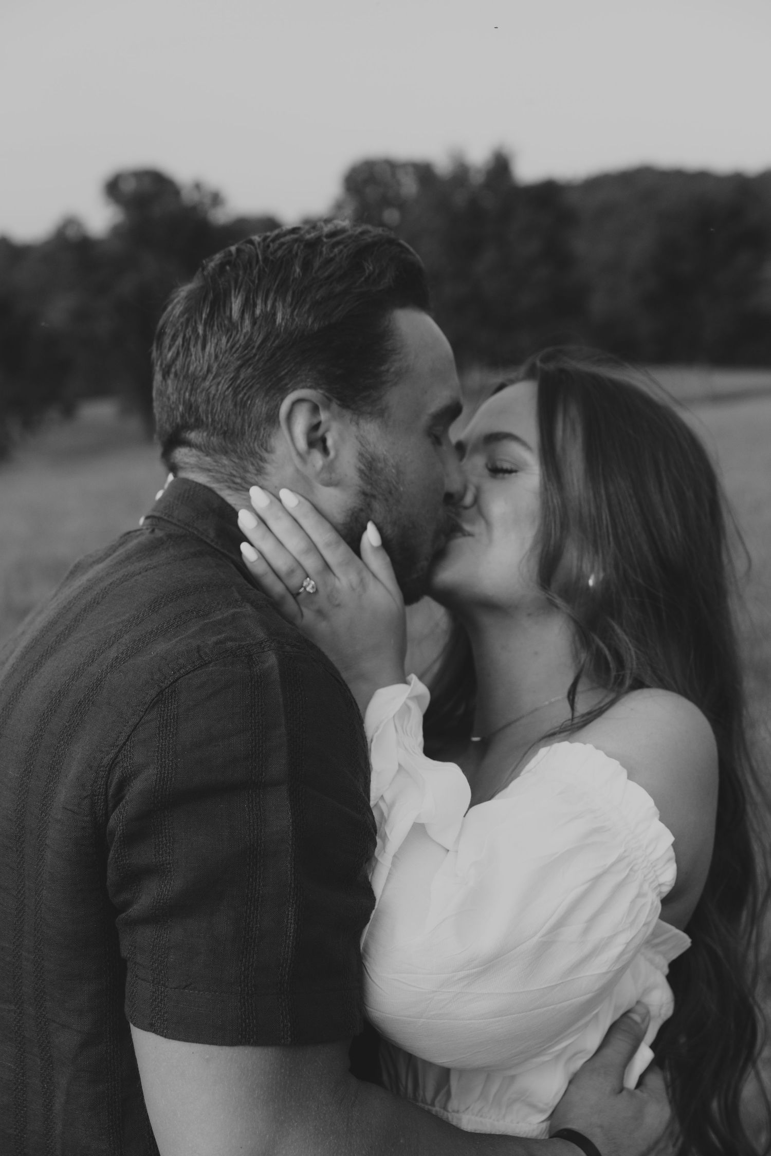 Black and white photo of a couple sharing a passionate kiss outdoors in a field.