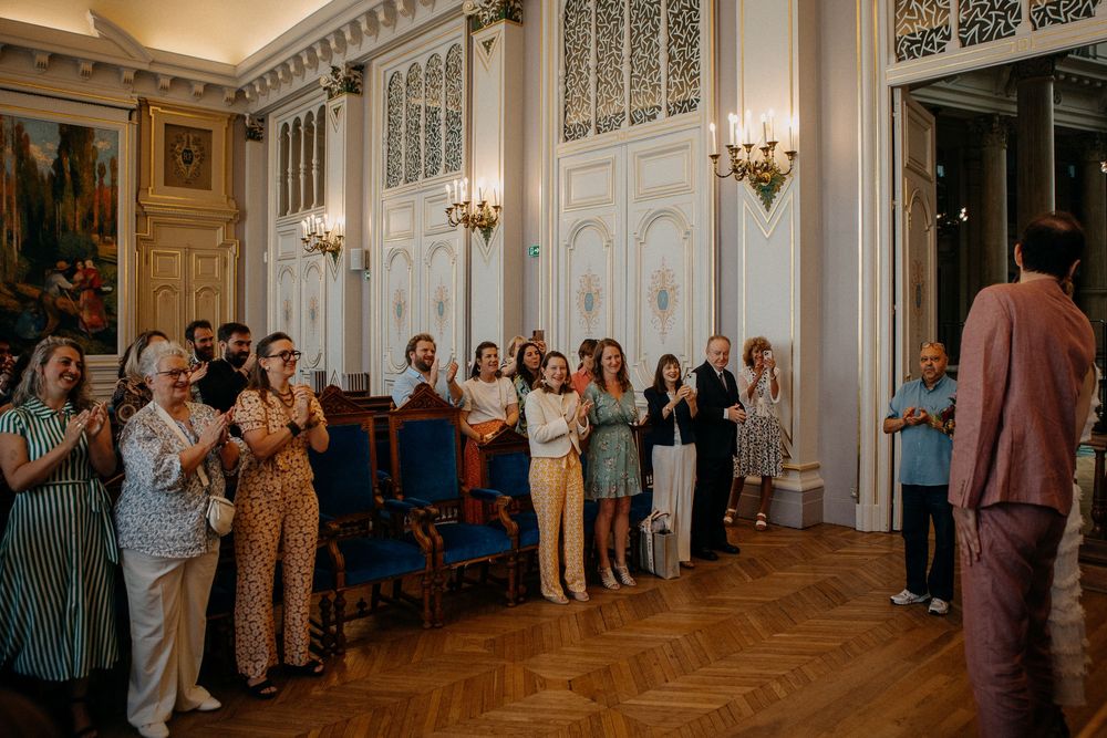 Guests applauding in an elegant white ballroom with ornate decor during a formal celebration or wedding reception.