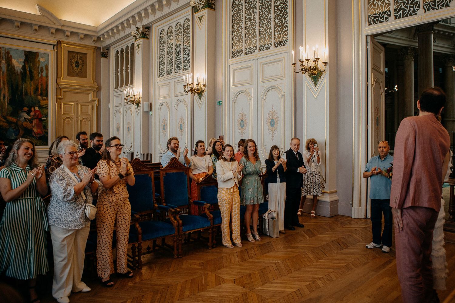 Guests applauding in an elegant white ballroom with ornate decor during a formal celebration or wedding reception.