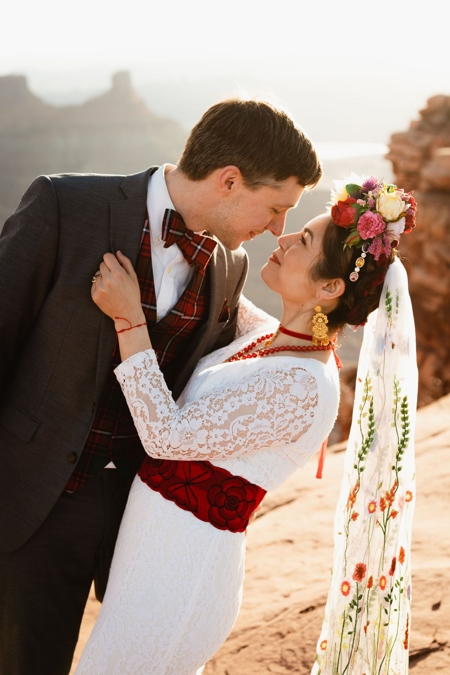 Couple in elegant wedding attire share romantic moment at golden hour in red rock canyon.