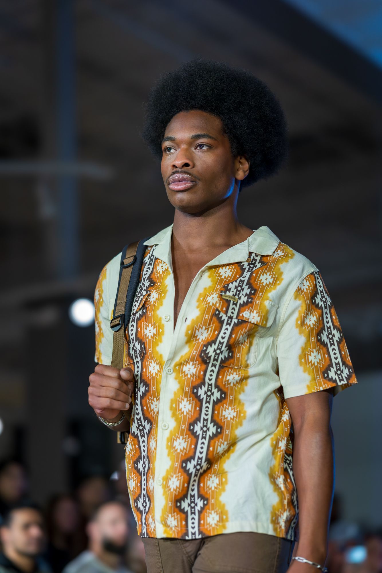 Male model walking runway in patterned African-inspired short sleeve shirt.