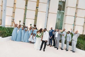 Wedding party in blue dresses and gray suits celebrating outdoors with bride and groom at a modern venue.