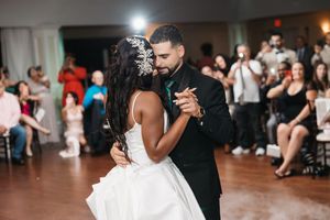 Bride and groom share their first dance at wedding reception, guests watching in background.