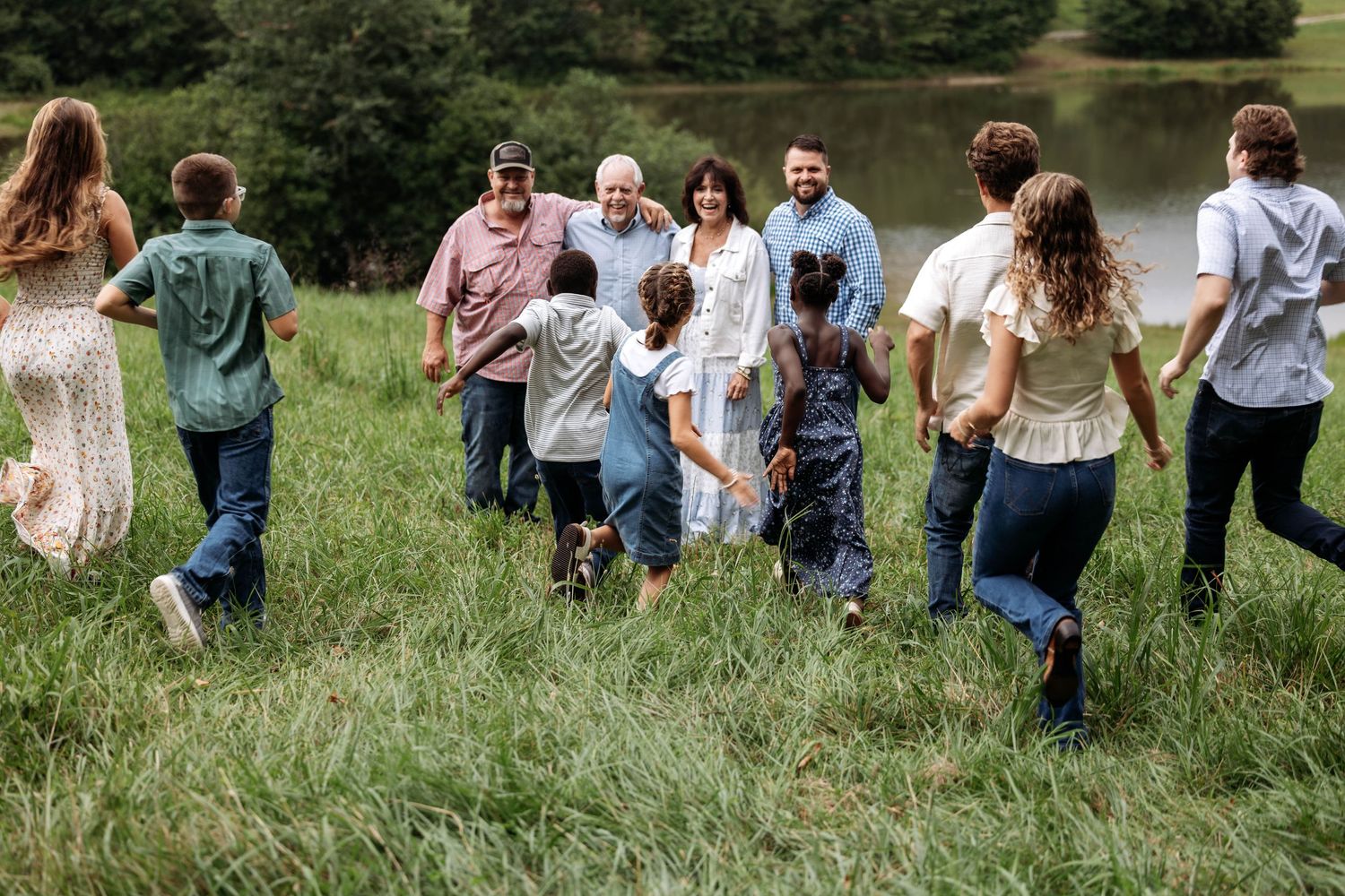 Large family walking together through green meadow near pond, multi-generational outdoor gathering on sunny day.