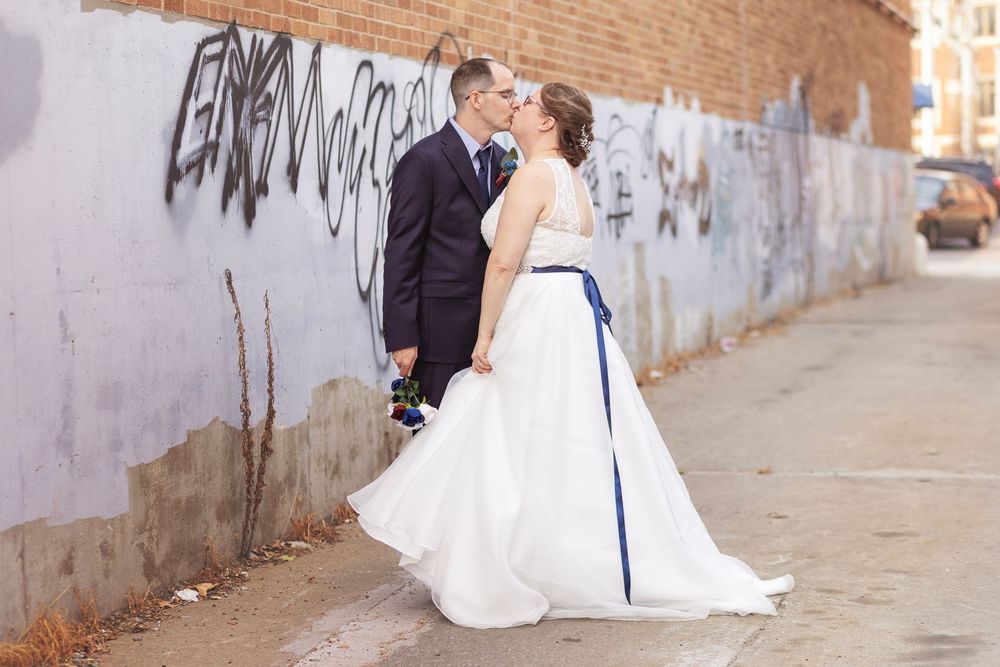 Bride and groom share a romantic kiss in front of a graffiti wall on their wedding day.