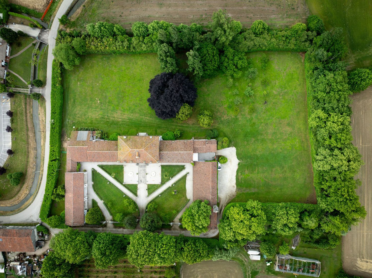 Aerial drone view of a rural estate with a historic building, manicured green lawns, and surrounding trees.