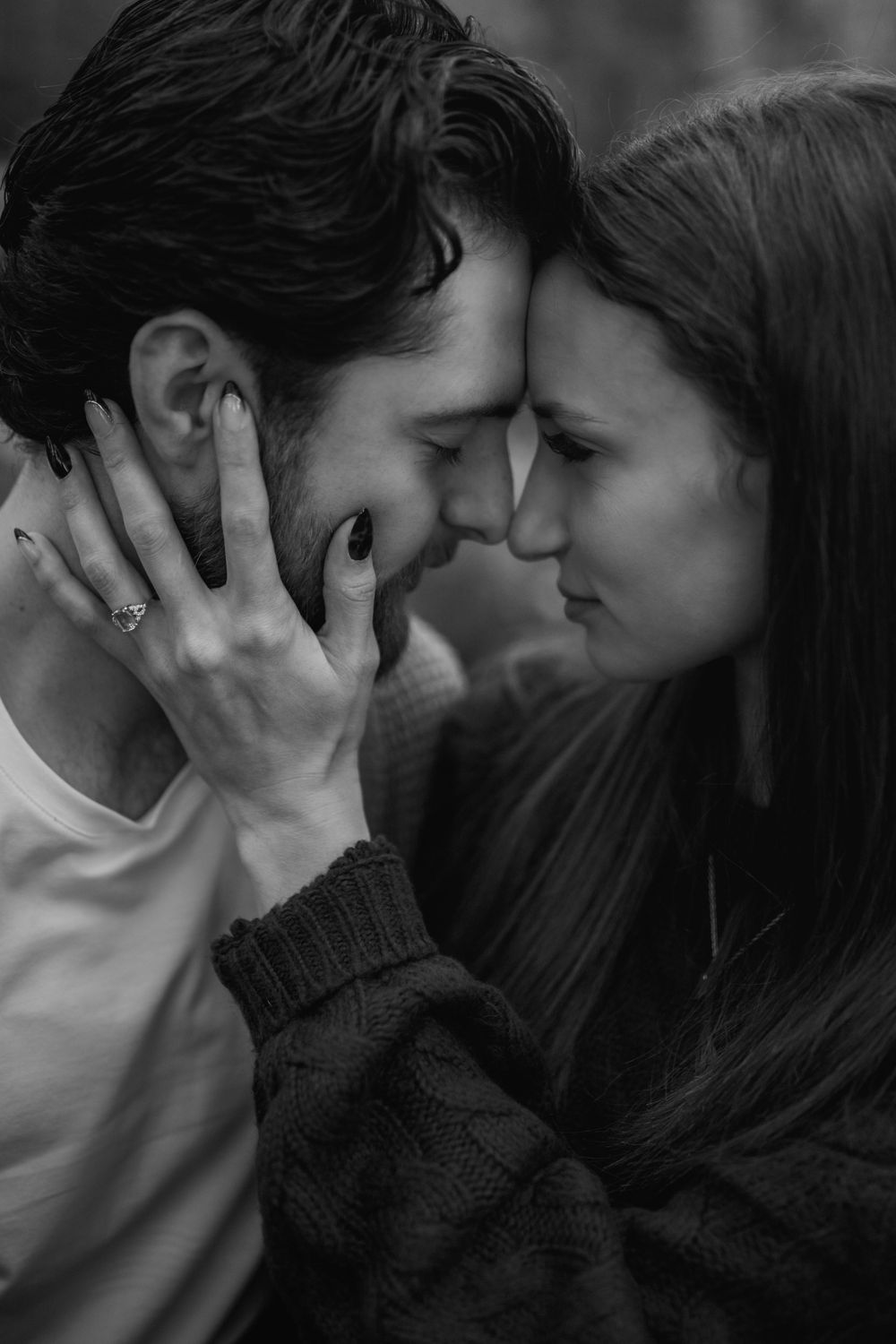 A black and white close-up of a couple touching foreheads as the woman gently cradles the man's face.