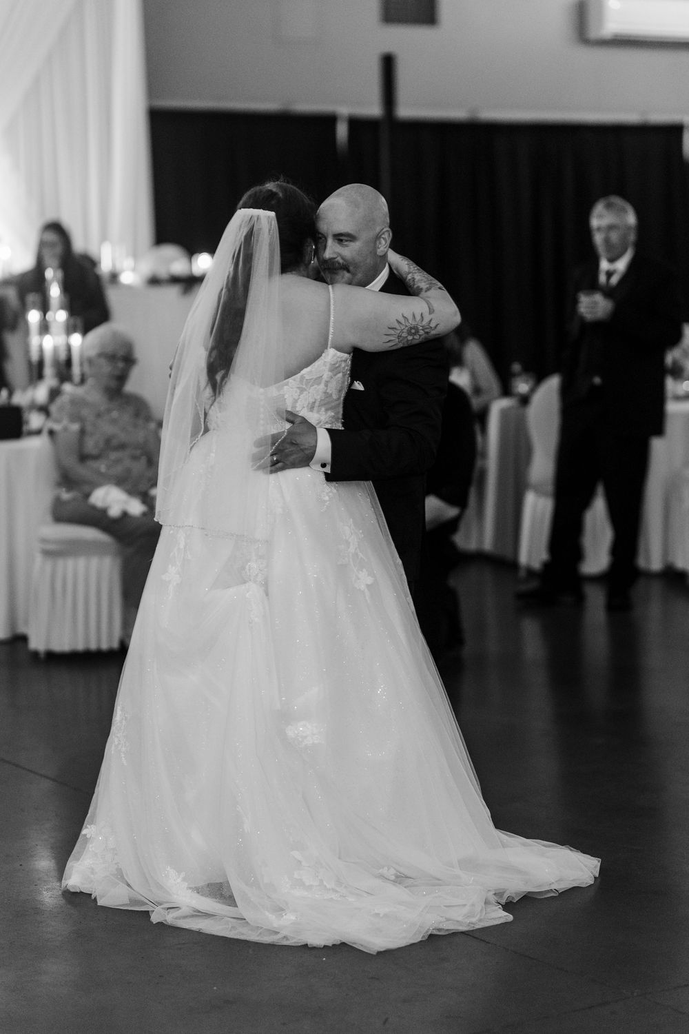 Black and white photo of a bride and groom sharing their first dance at a wedding reception.