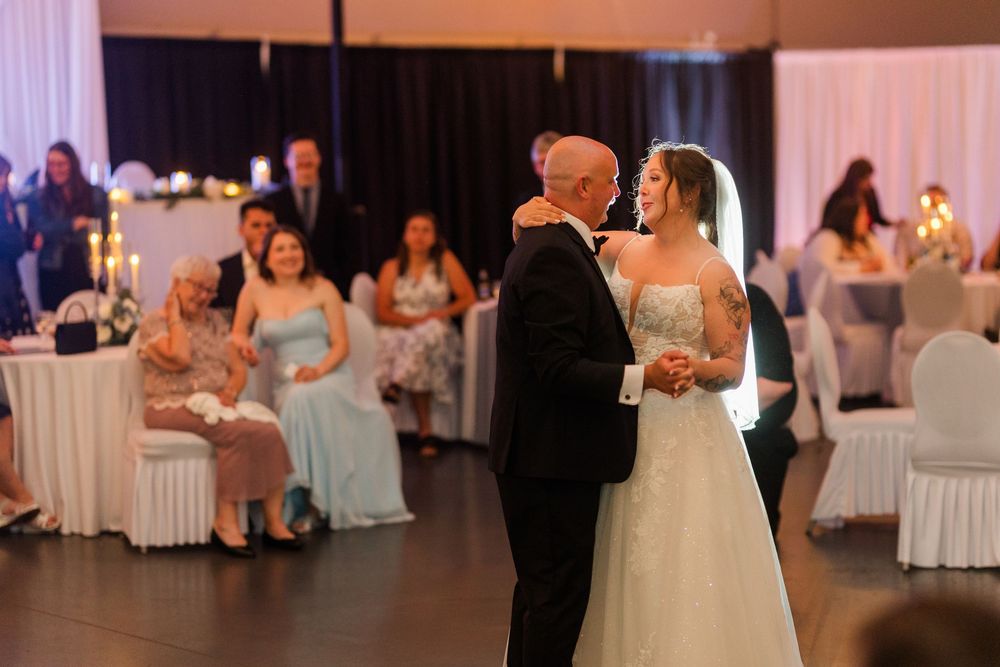Bride and her father share an emotional first dance at a elegant wedding reception with guests watching in the background.