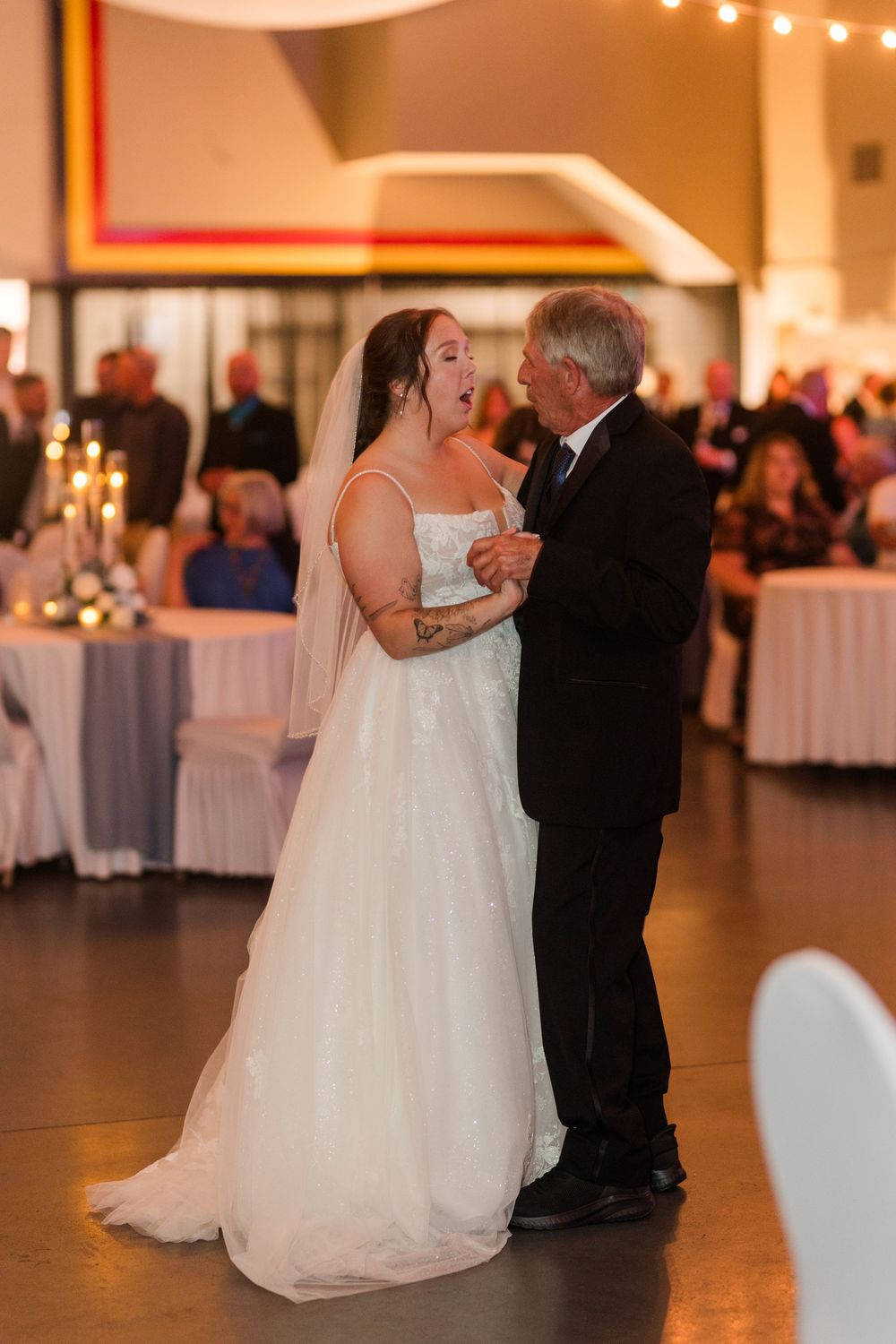 Bride in white gown and veil shares emotional father-daughter dance at elegant wedding reception.