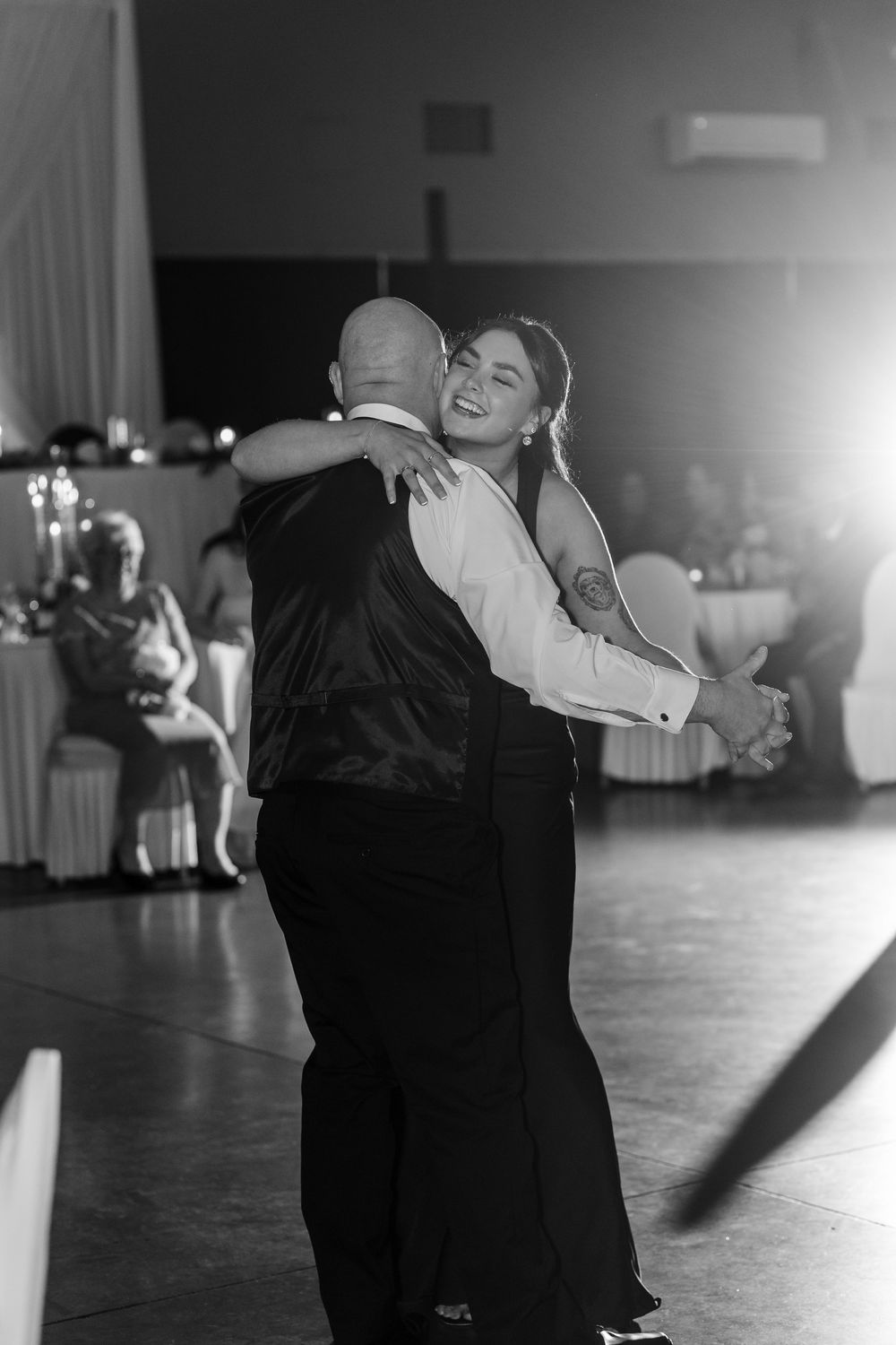 Black and white photo of bride smiling while sharing first dance with groom at wedding reception.
