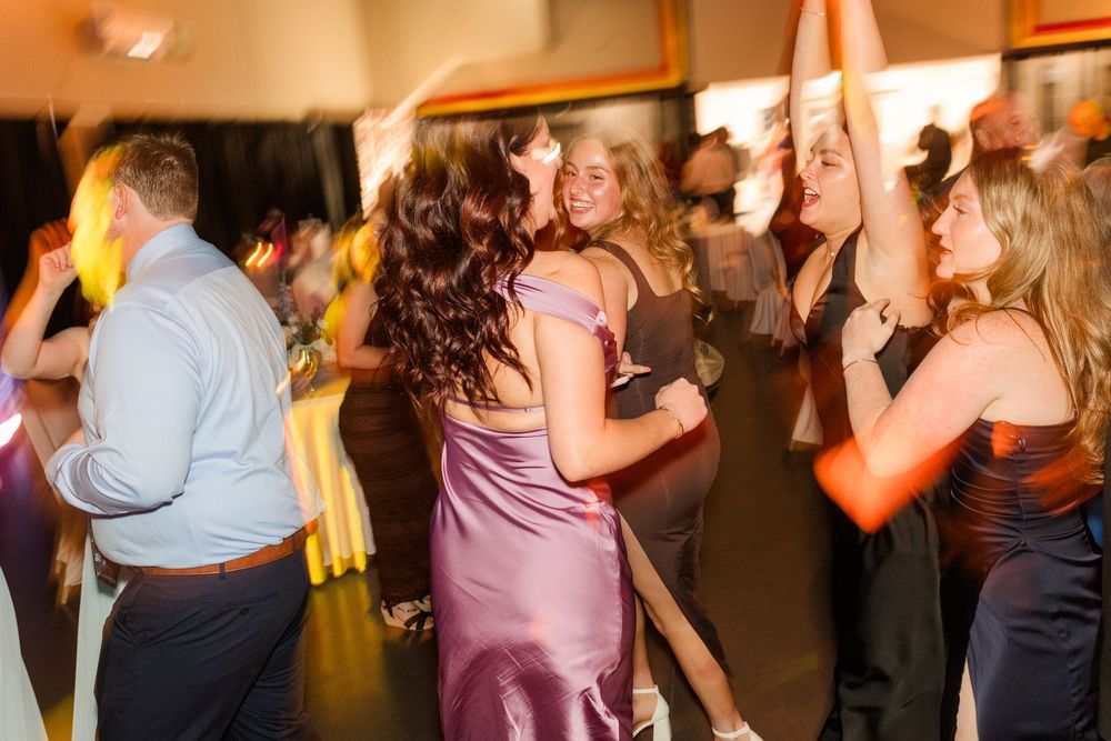 Guests dancing together at a formal wedding reception in elegant evening gowns under warm lighting.