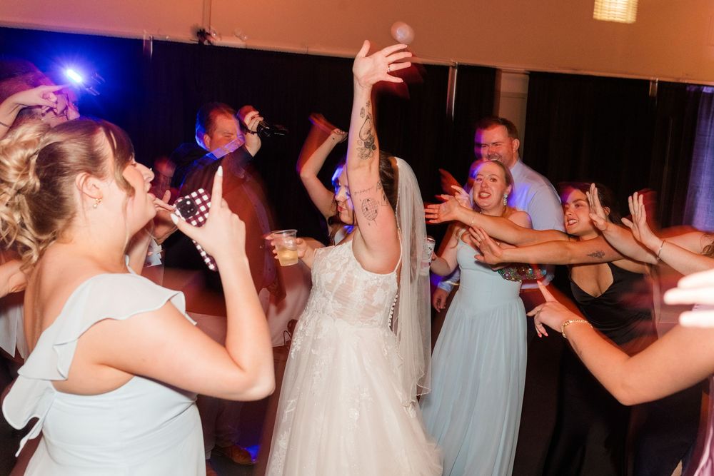 Bride in white gown dancing joyfully with guests at a lively wedding reception party.