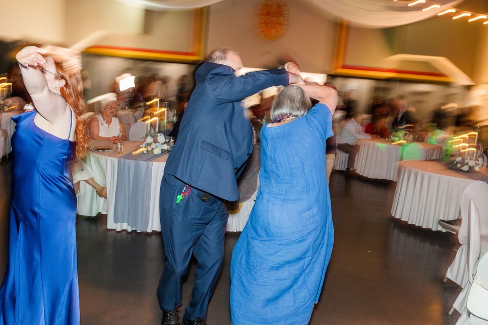 Guests dancing together at a wedding reception in a decorated banquet hall, wearing formal blue attire.