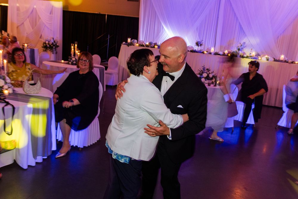 Couple sharing a romantic dance at an elegant wedding reception with white drapes and floral decorations.