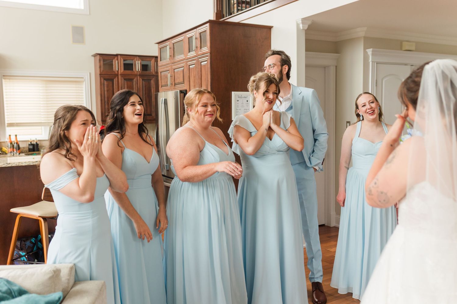 Bridesmaids in light blue gowns react with tears and joy seeing the bride for the first time on her wedding day.