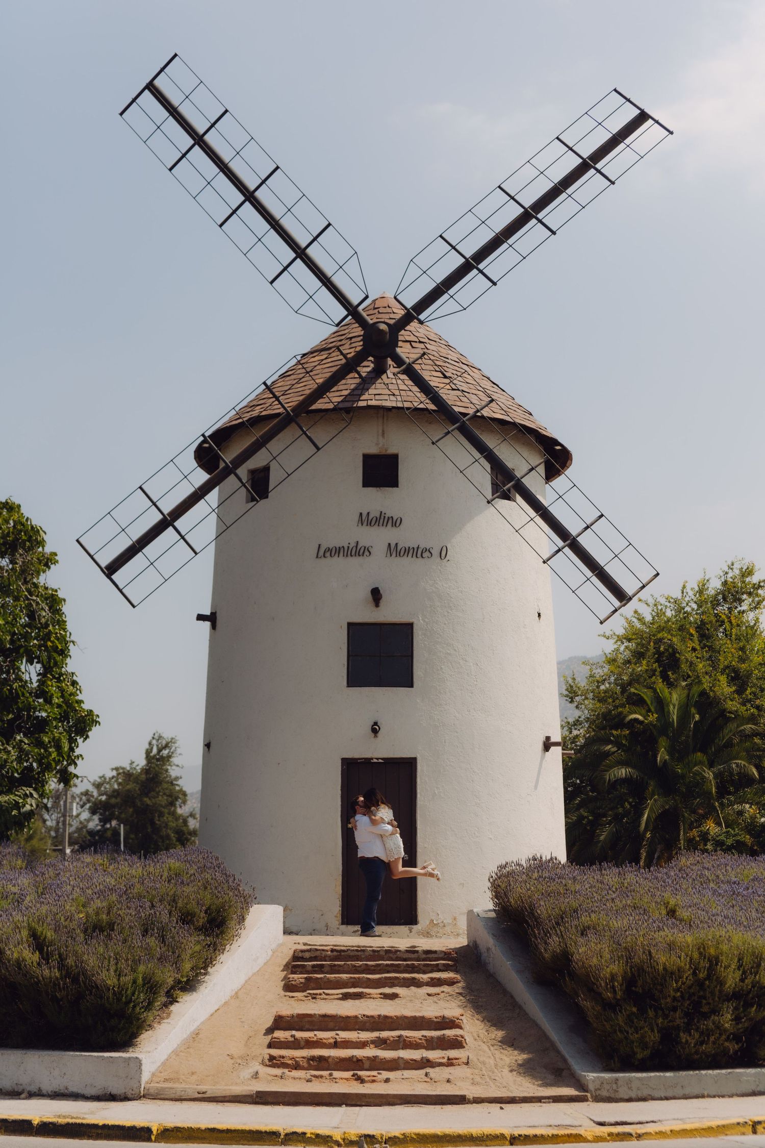 Couple posing in front of a charming white windmill named Molino Leonidas Montes outdoors.