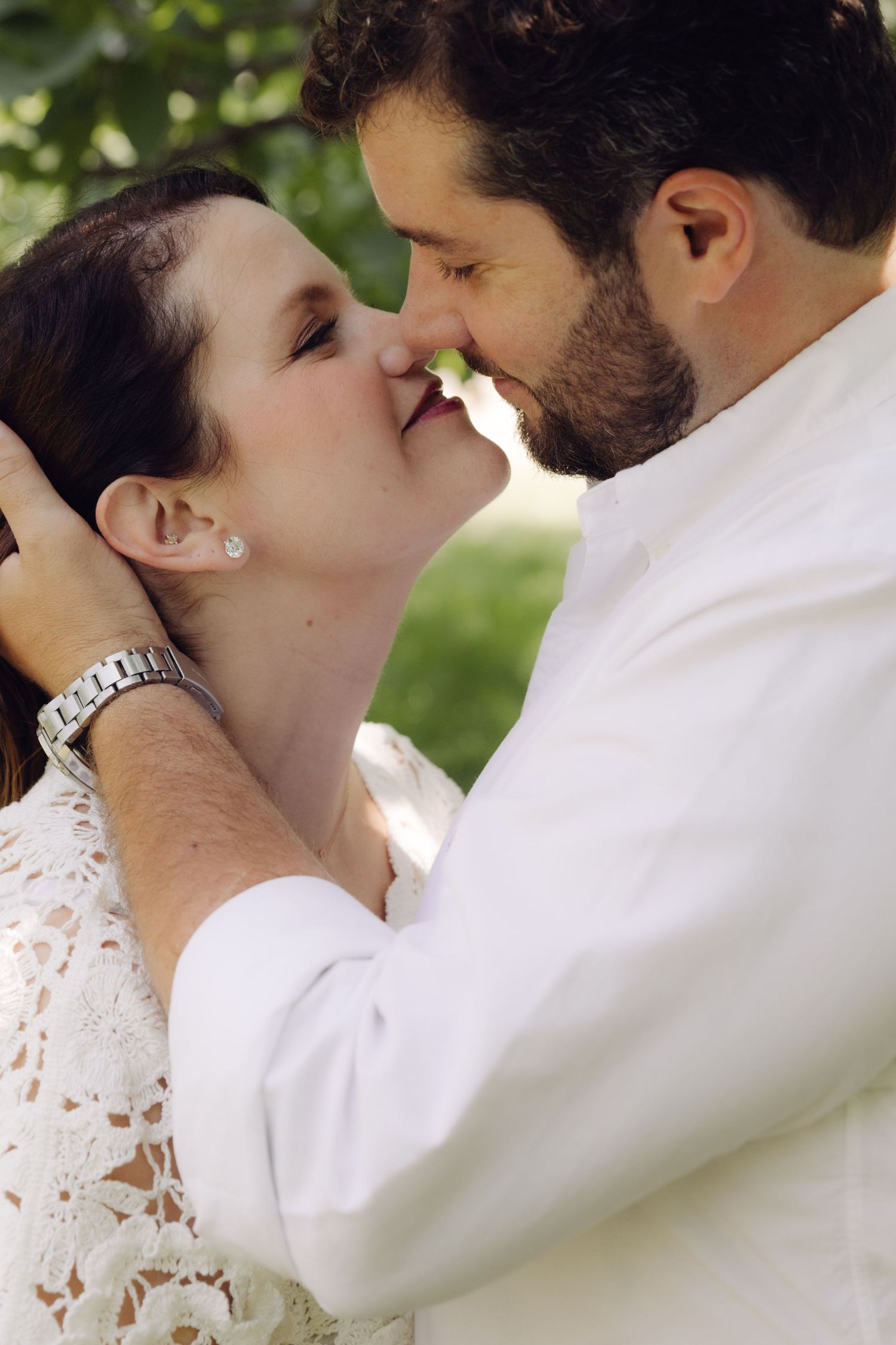 Close-up of couple sharing a tender nose-to-nose moment, man cradling womans face gently outdoors.
