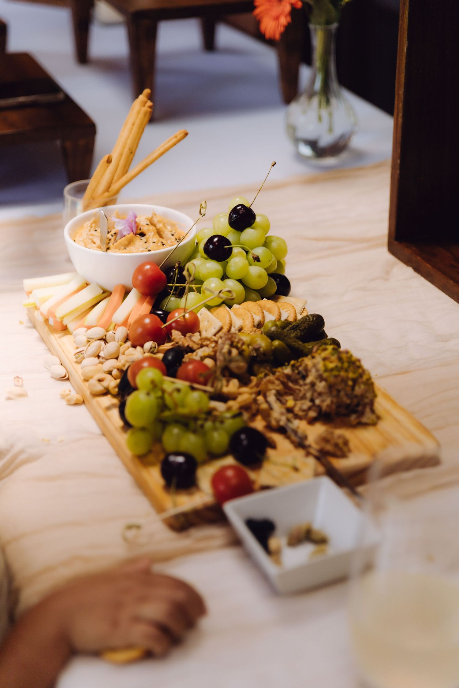 Elegant charcuterie board with grapes, cherry tomatoes, nuts, and crackers arranged on wooden serving board.
