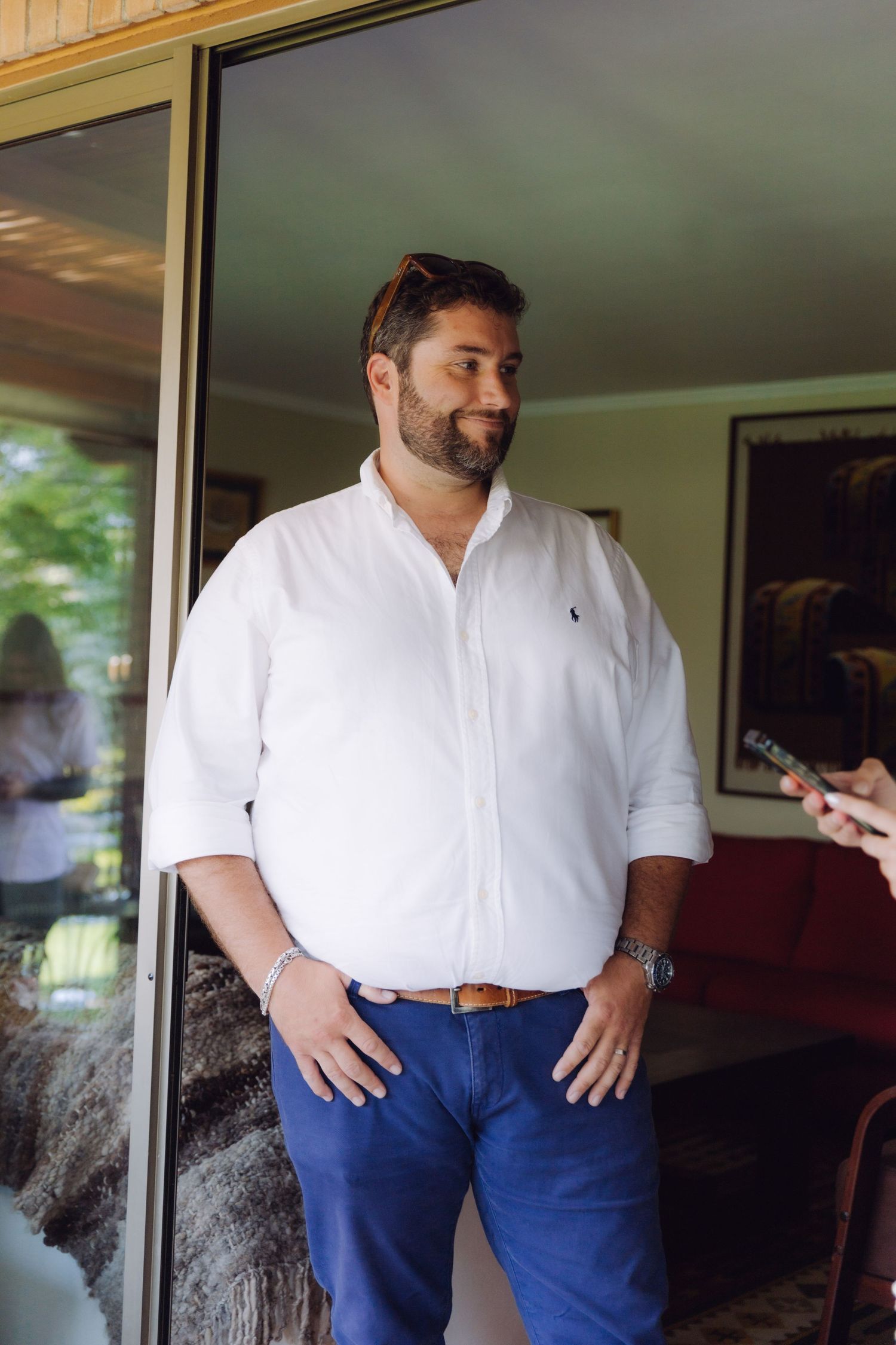 A bearded man in a white polo shirt stands confidently in a glass doorway.