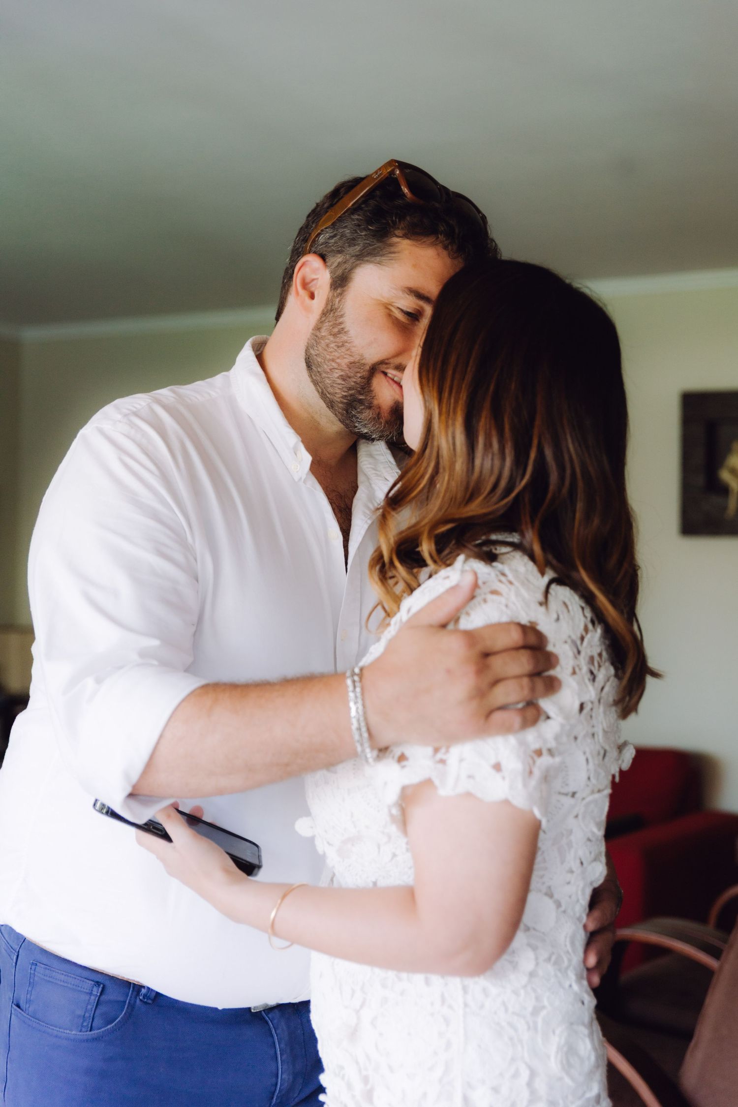 A couple shares a tender embrace indoors, man in white shirt holding phone.