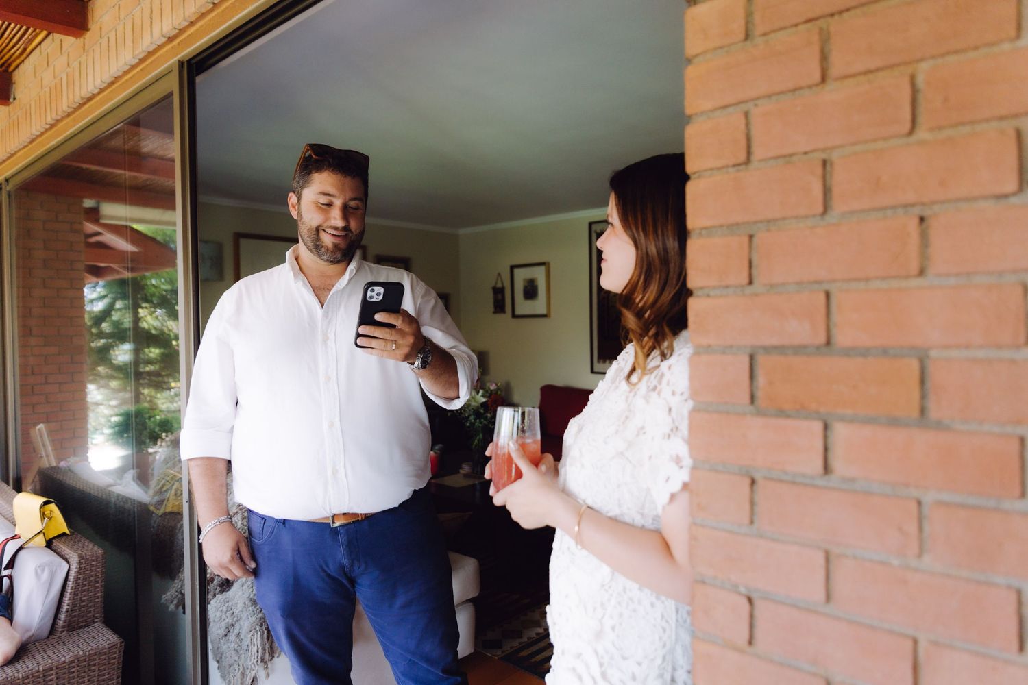 A man and woman share a lighthearted moment on a brick porch with drinks.