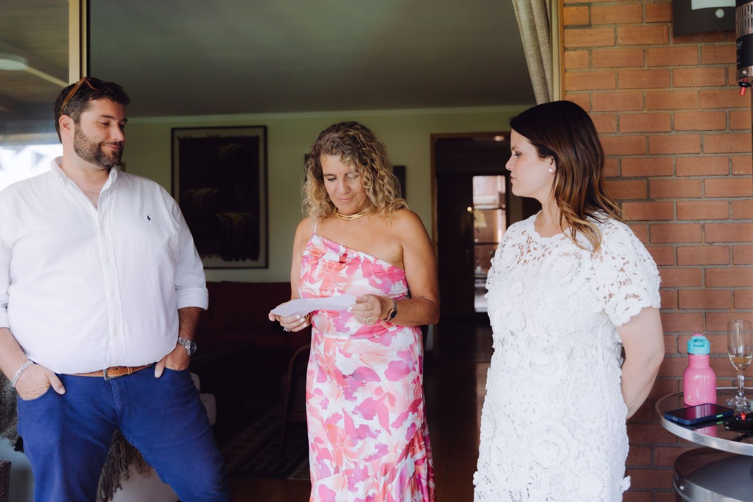 Three guests chatting at a wedding, woman in pink floral dress holding a card between two others.